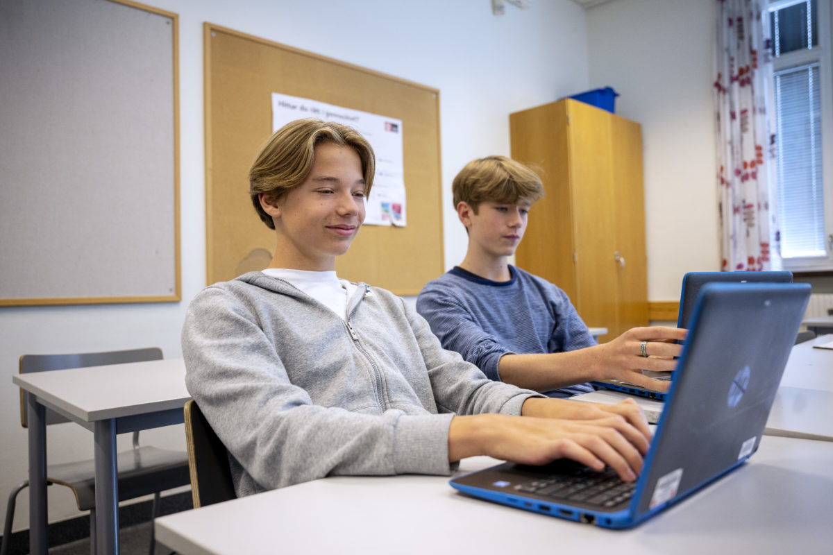 Två killar skriver på en varsin laptop i skolan.