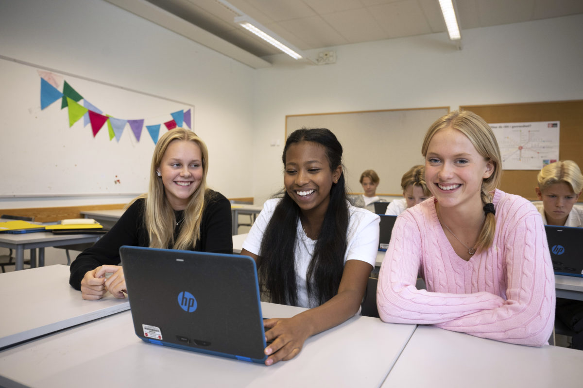 Tre glada tjejer surfar på sin laptop i skolan.