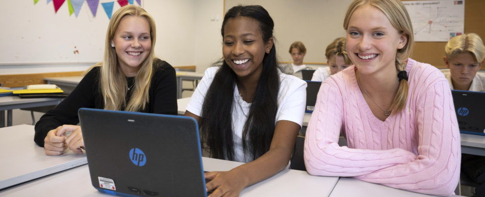Tre flickor sitter vid skolbänken med en laptop framför sig.